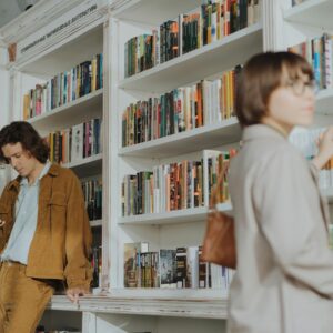 Two people browsing books in a cozy bookstore. A man checks his phone while a woman selects a book.