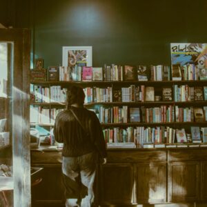 A person standing indoors, browsing books in a cozy bookstore with wooden shelves.